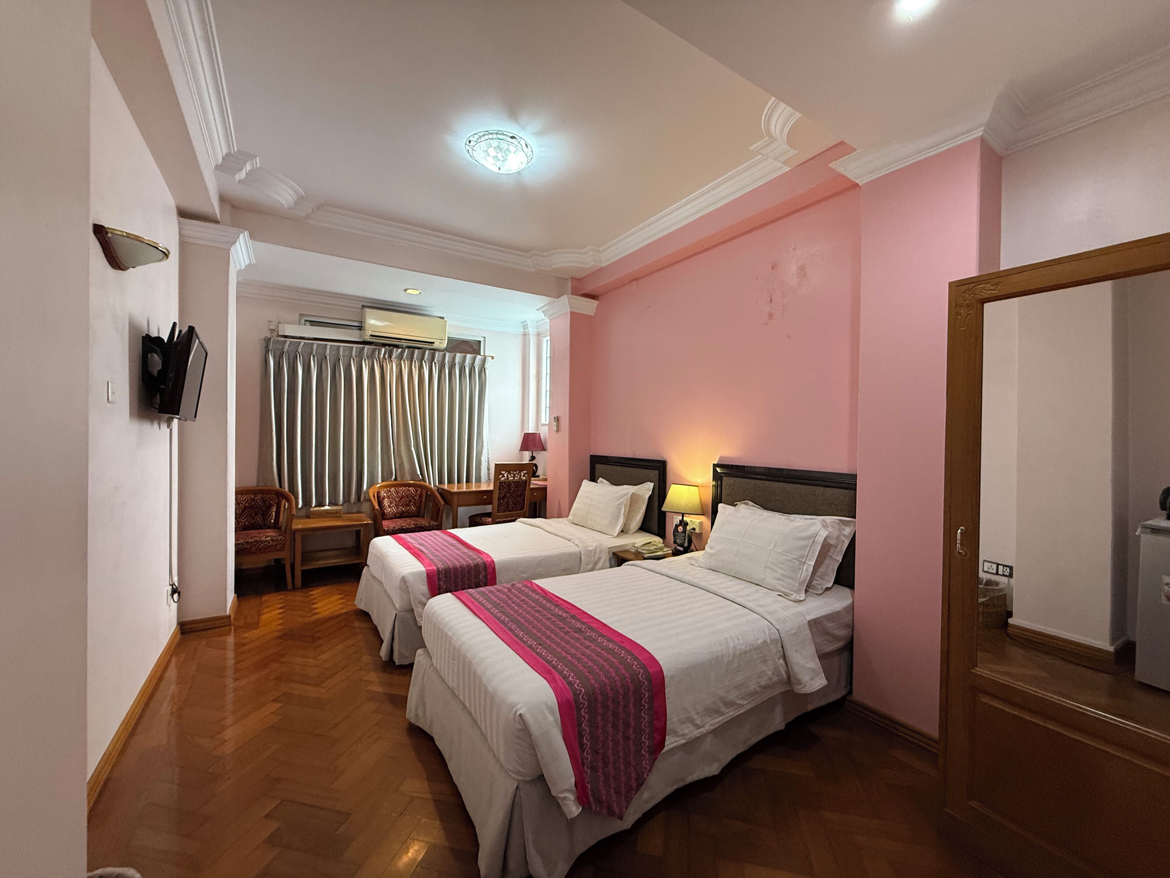 A hotel room with two beds, a desk, a chair, a mirror, and a wardrobe.