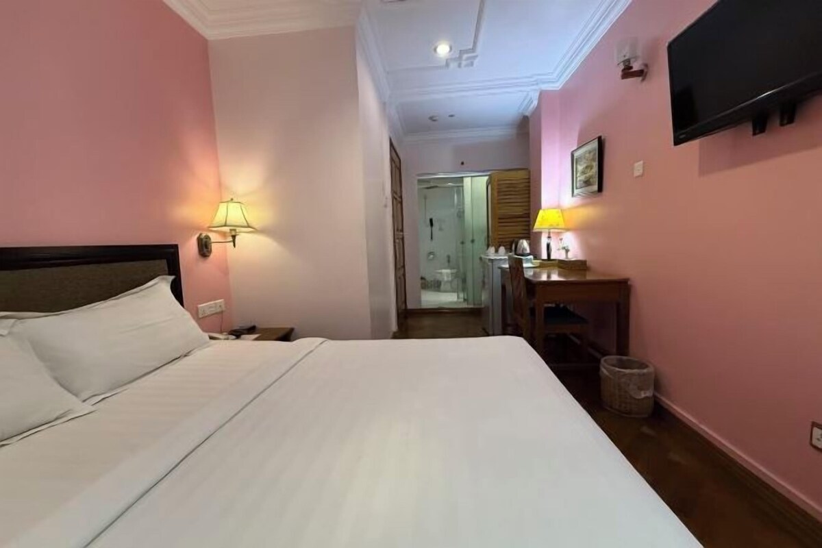 A hotel room with a large bed, a desk with a lamp, and a television on the wall.