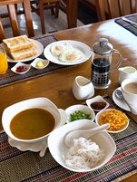 Una mesa de desayuno con tostadas, huevos fritos, una cafetera y diferentes condimentos.