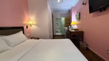 Una habitación de hotel con una cama grande, un escritorio con lámpara, un televisor en la pared y un baño visible a través de una puerta abierta.