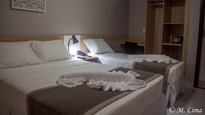 A hotel room with two beds, a nightstand with a lamp, a telephone, and a wooden wardrobe. - Hotel Enseada Aeroporto (Recife)
