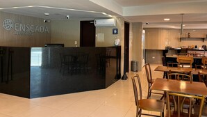 A hotel reception area with a modern design, featuring a reception desk, seating area, and a kitchenette in the background. - Hotel Enseada Aeroporto (Recife)