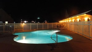 A nighttime pool area with a curved pool, a metal ladder, and a white fence. - Sea Esta Motel II (Millsboro)