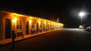 A row of log-style cabins with outdoor seating, illuminated by warm lighting. - Sea Esta Motel II (Millsboro)