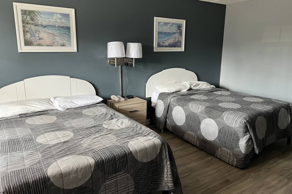 A hotel room with two beds, a nightstand with a lamp, and two framed pictures on the wall.