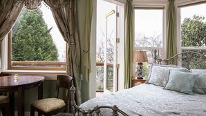 A bedroom with a large bed, a round table, and a chair, with a view of trees through the window.