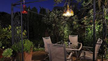 An outdoor patio with a table and chairs, surrounded by greenery and a decorative metal structure.