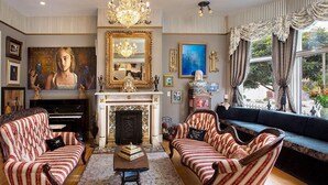 A room with a grand piano, two striped armchairs, a fireplace, and a large painting.
