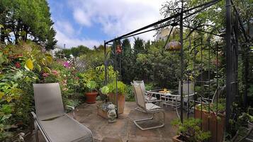 A patio with a table and chairs, surrounded by potted plants and a variety of flowers.