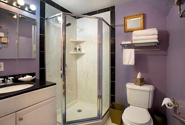 Un baño con ducha de vidrio, inodoro blanco, lavamanos con encimera negra y espejo con luces arriba.