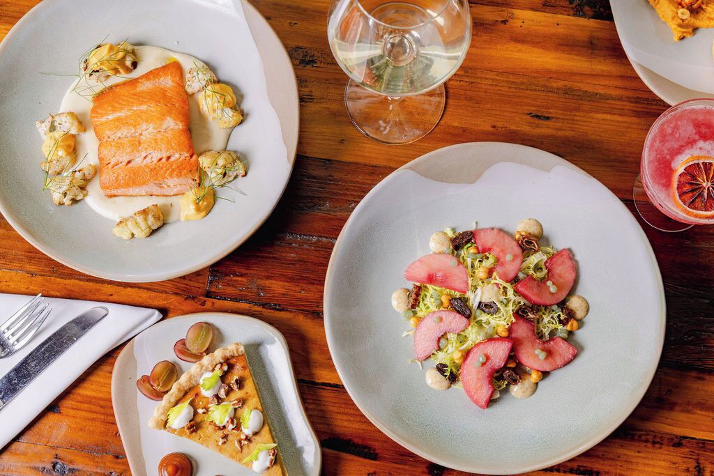 A dining table with plates of food, a glass of white wine, and a dessert plate.