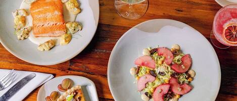 A dining table with plates of food, a glass of white wine, and a dessert plate.