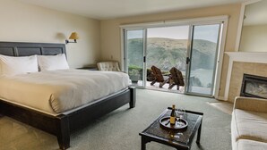 A hotel room with a large bed, a sofa, a small table with a bottle and glass, and a view of the ocean through a sliding door. - SCP Mendocino Coast Lodge  (Albion)
