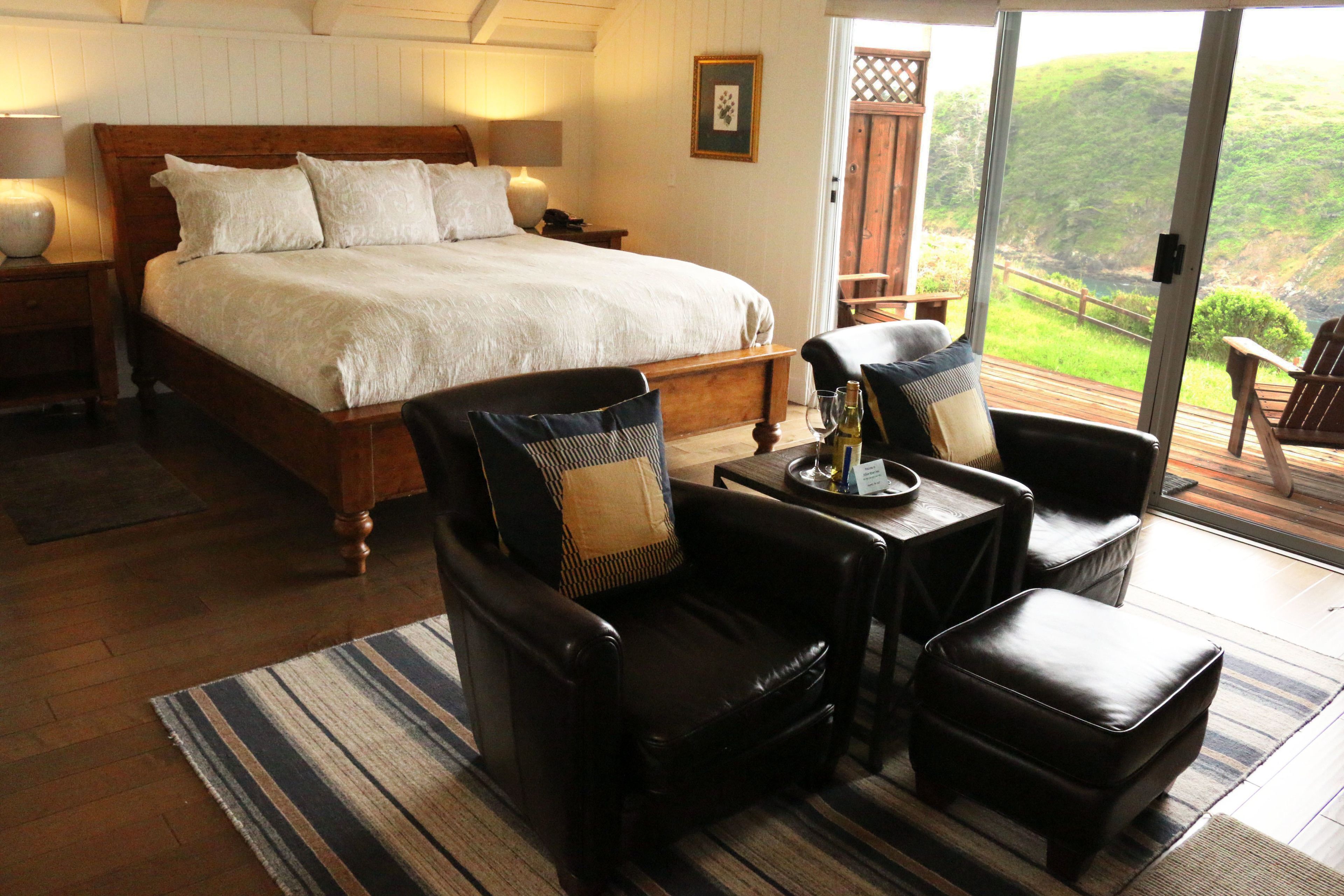 Une chambre dotée d’un grand lit, de deux fauteuils, d’une petite table et offrant une vue sur un paysage luxuriant grâce à une porte coulissante.