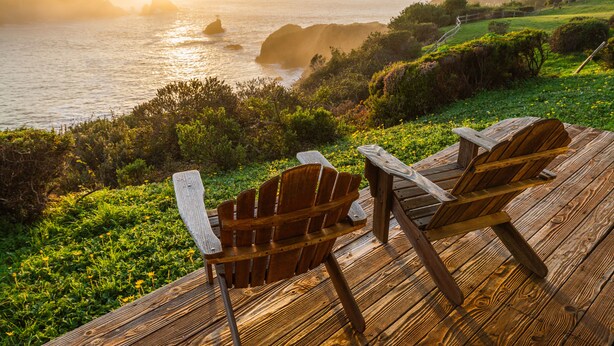 A wooden deck with two Adirondack chairs overlooking a coastal landscape with hills and the ocean. - SCP Mendocino Coast Lodge  (Albion)
