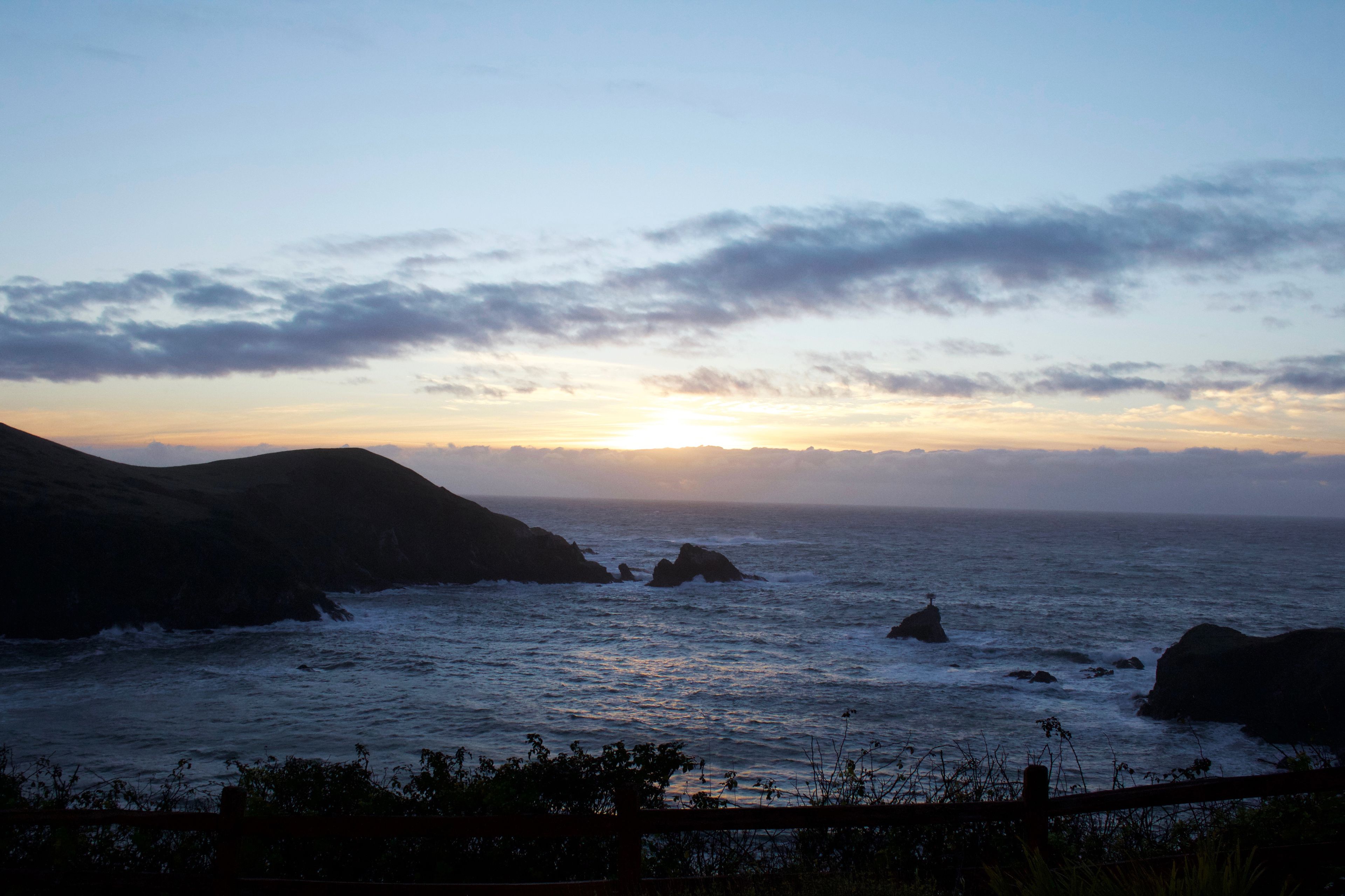 A coastal landscape with rocky outcrops and the ocean at sunset.
