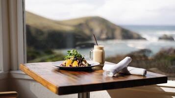 Une table dressée avec un repas et une boisson, donnant sur un paysage côtier.