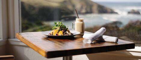 A table with a meal and a drink, overlooking a coastal landscape.