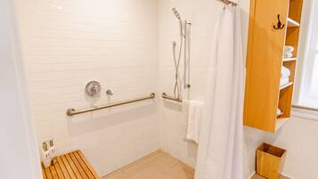 Un baño moderno con paredes de azulejos blancos, un banco de madera, una ducha con puerta de cristal y un armario de madera con estantes.