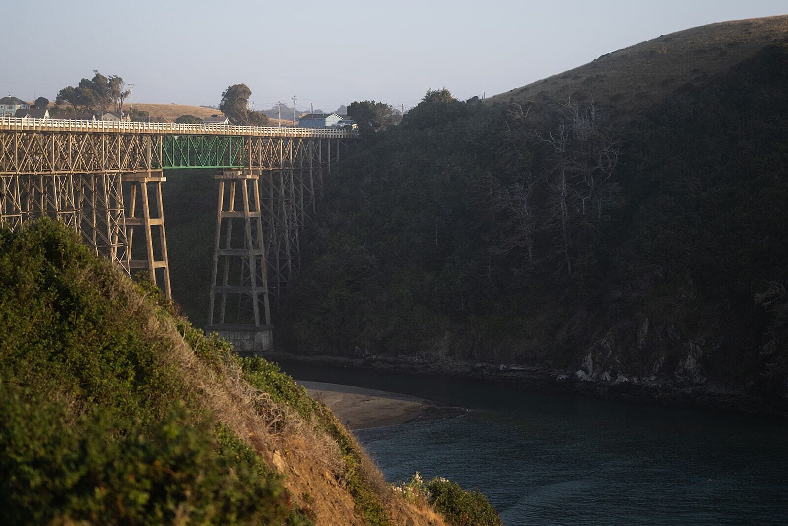 A coastal bridge with a wooden structure and a green railing.