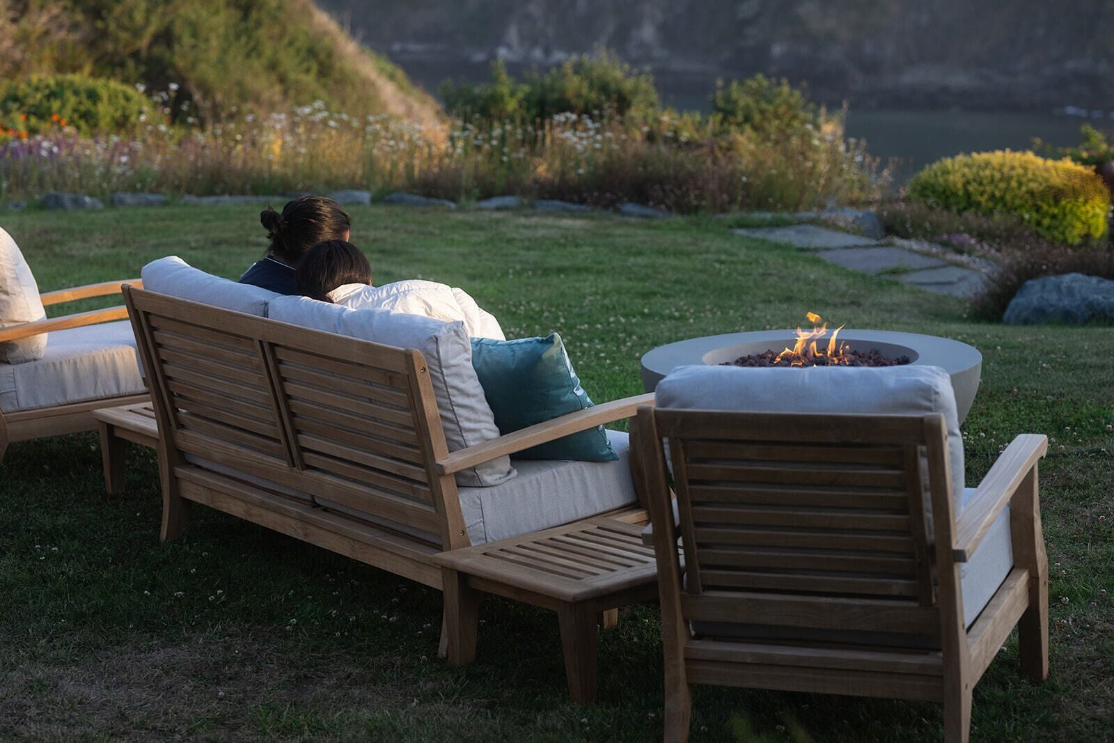 A wooden bench with cushions and a fire pit in a garden setting.