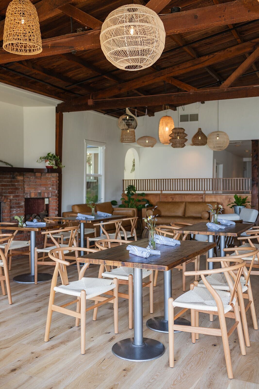 A restaurant interior with wooden tables and chairs, a brick fireplace, and hanging wicker lamps.
