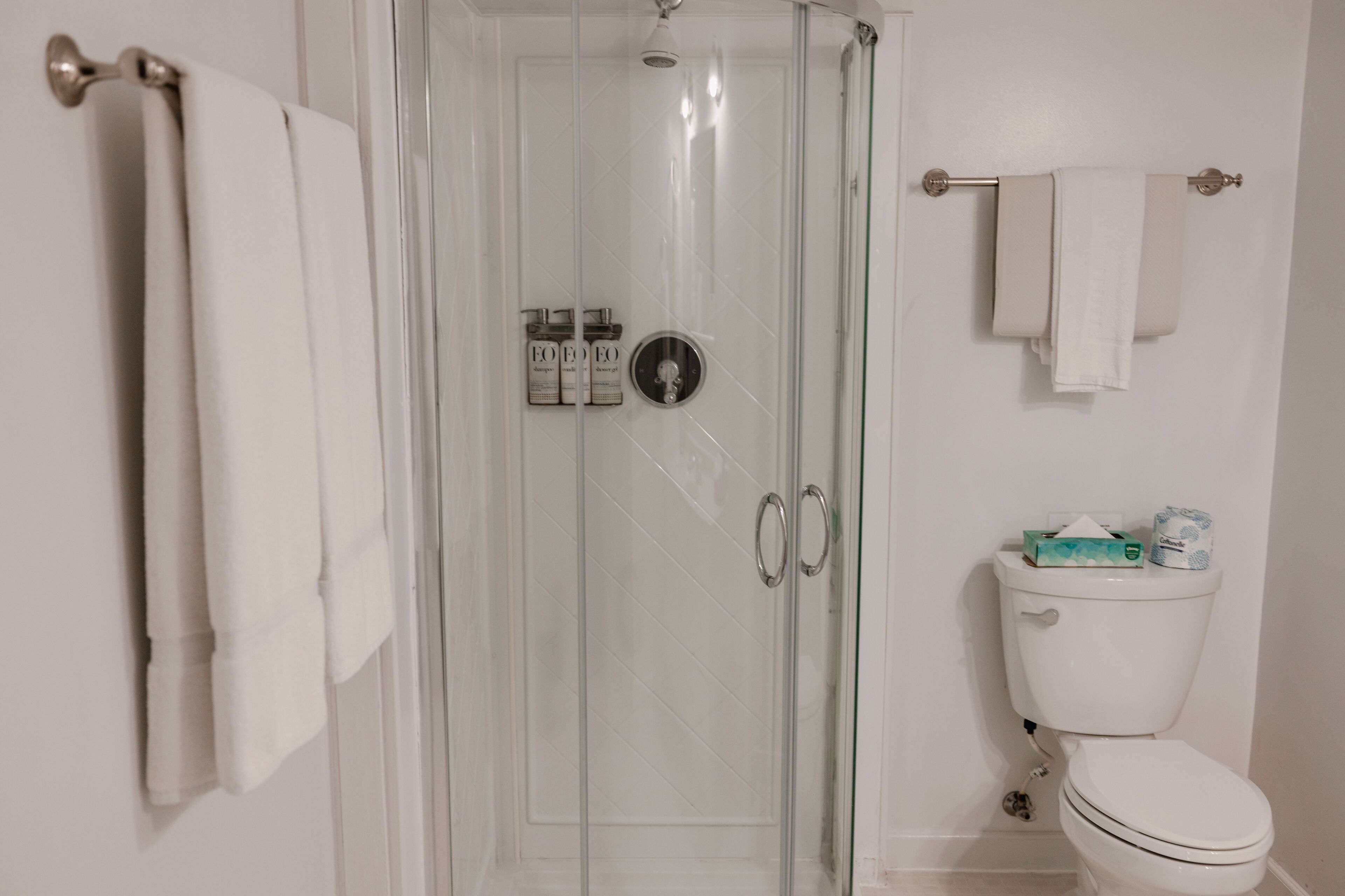Un baño con mampara de vidrio, un inodoro y dos barras para toallas.