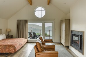 Ein Schlafzimmer mit einem großen Bett, einem Kamin, Blick durch ein Fenster und einem Balkon mit Sitzgelegenheiten.