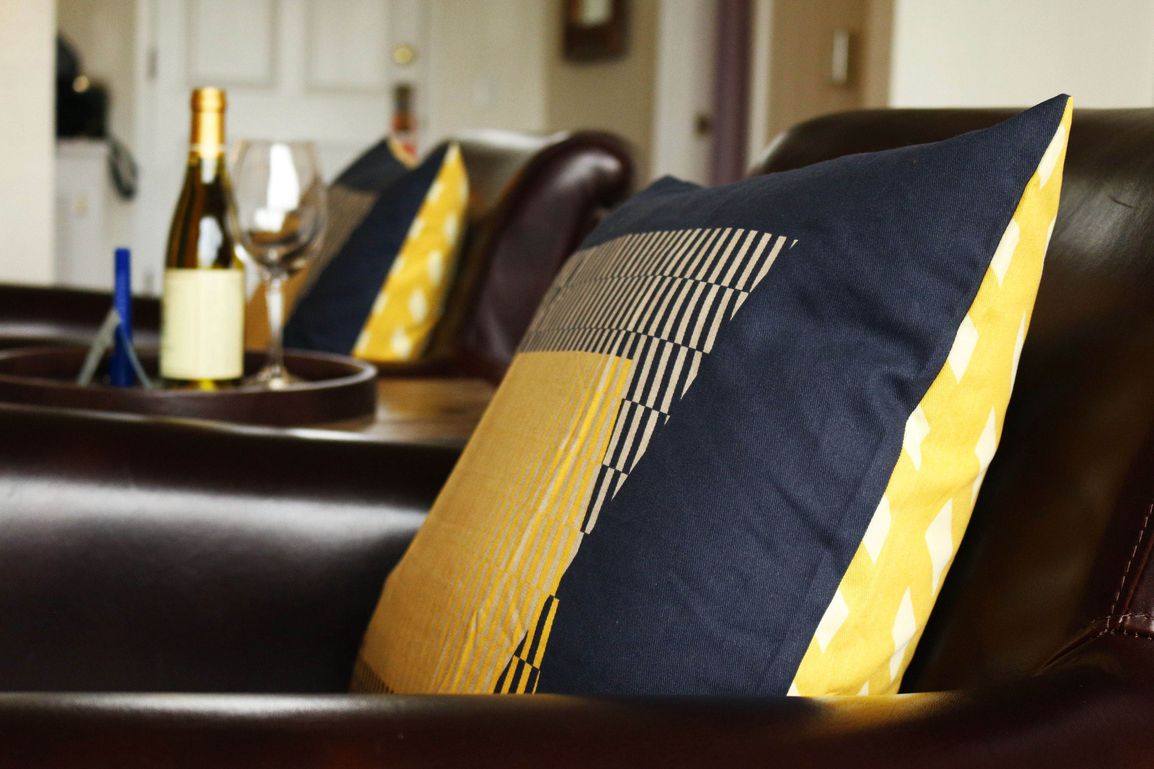A dark brown leather sofa with a decorative pillow featuring a geometric pattern and a yellow and white striped design.