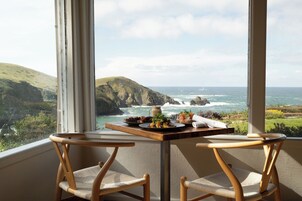 Un balcón con una mesa dispuesta para dos personas, con vistas a un paisaje costero con acantilados y el mar.