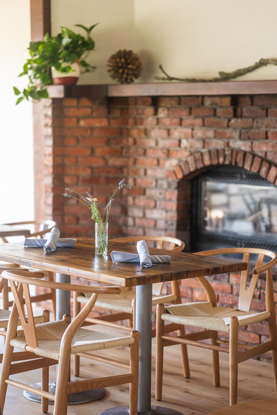 Una chimenea de ladrillo con repisa, una mesa de comedor con sillas y una planta en maceta.