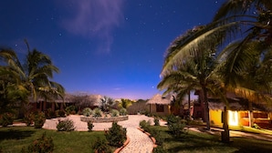 A nighttime view of a resort with thatched-roof buildings, palm trees, and a starry sky. - Cabañas El Cielito (Villa del Mar)