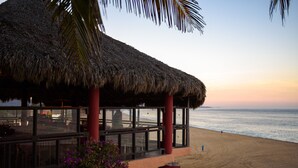 A beachside building with a thatched roof and large windows overlooking the ocean. - Cabañas El Cielito (Villa del Mar)
