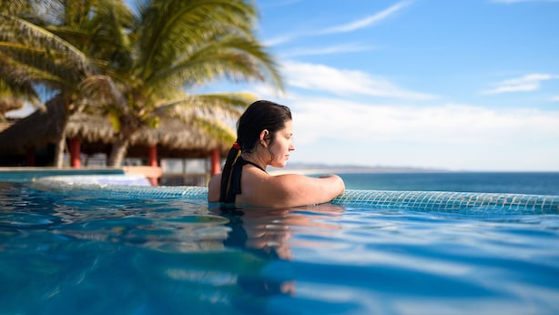 A person in a swimming pool with a view of the ocean and palm trees. - Cabañas El Cielito (Villa del Mar)