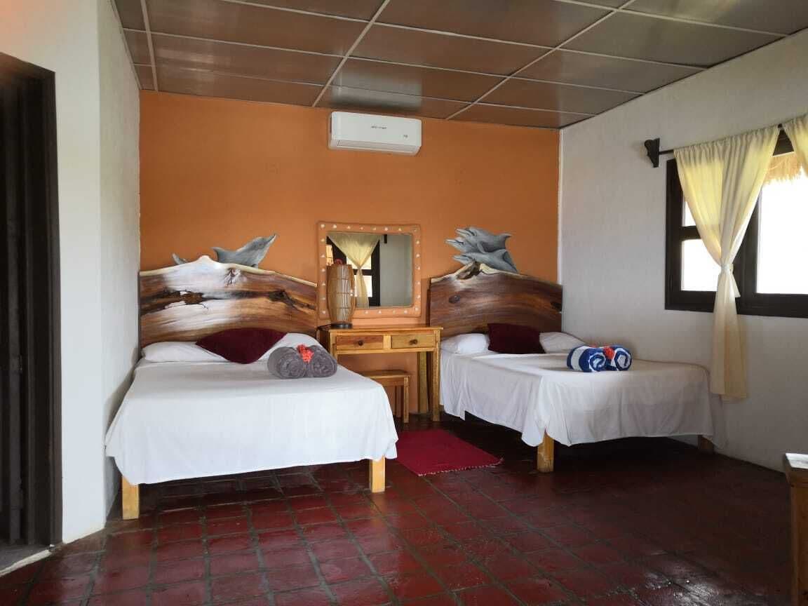 A room with two beds, a wooden desk, a mirror, and a window with curtains.