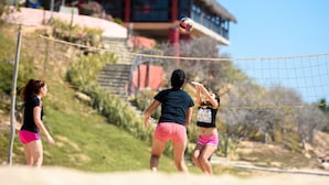 A beach volleyball game with players in the foreground and a thatched-roof building in the background. - Cabañas El Cielito (Villa del Mar)