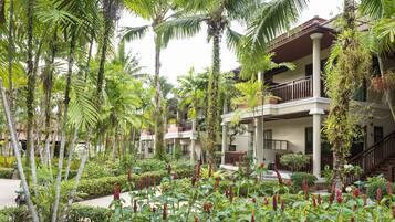 Un resort con edificios de varios pisos, abundante vegetación tropical y un jardín cuidado con flores rojas.