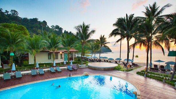 A swimming pool with lounge chairs and umbrellas, surrounded by palm trees and a view of the sea. - Khaolak Bay Front Resort (Takua Pa)