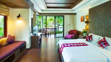 A hotel room with a bed, a desk with a computer, a chair, a sofa, and a view of a pool and palm trees.