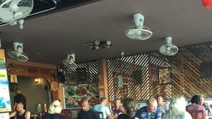Ravintolassa on puupöydät ja -penkit, kattoon asennetut tuulettimet ja laattalattia.