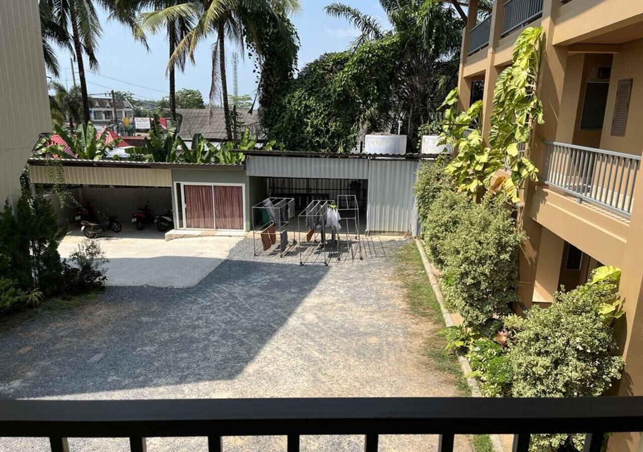 A building with a covered outdoor area, a small garden, and a balcony with a railing.