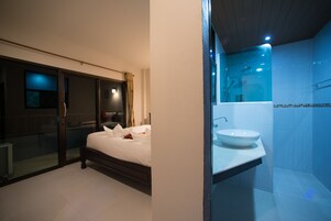 Un dormitorio con cama, puerta de cristal que da a un balcón y baño con lavamanos y ducha.