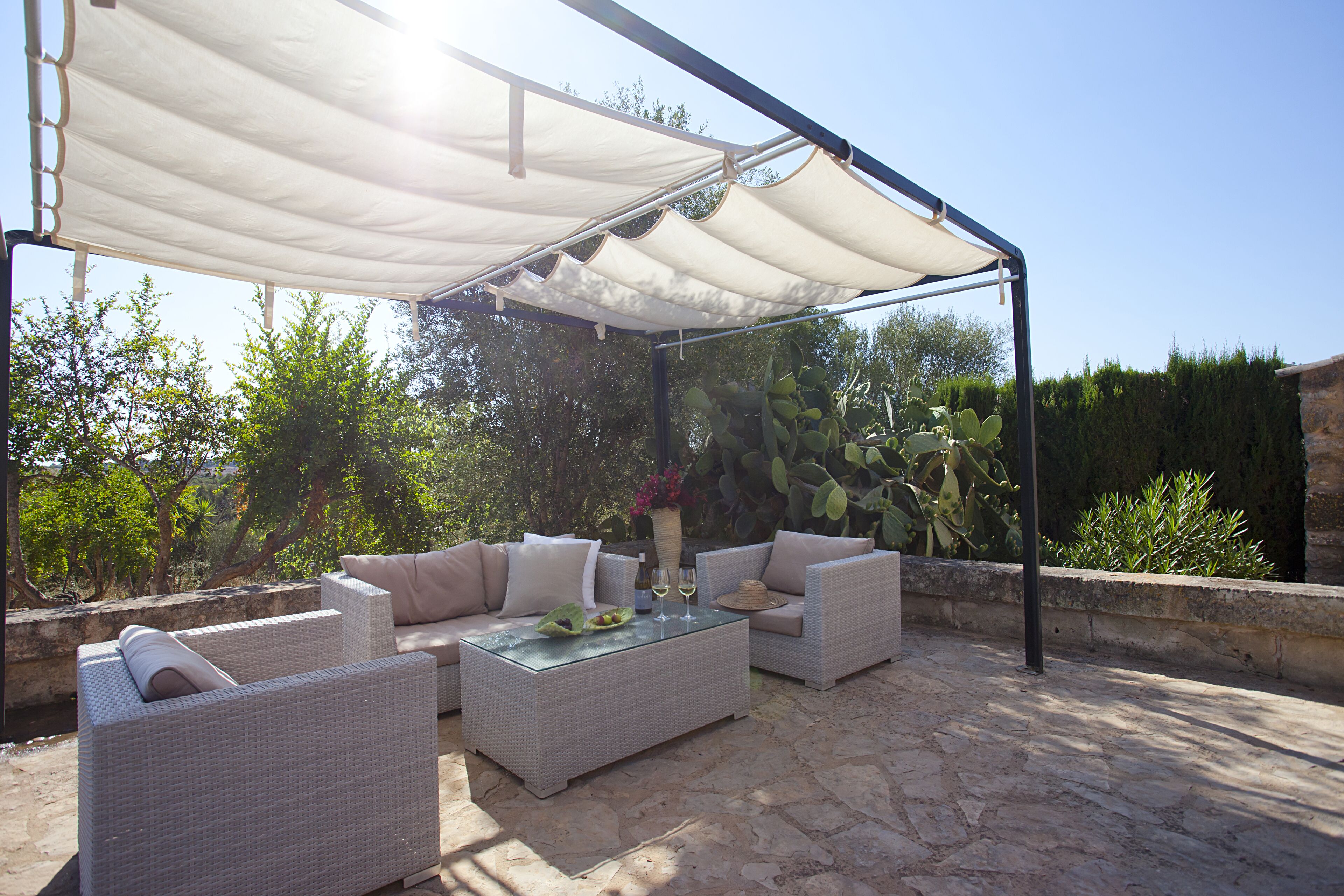 An outdoor patio with wicker furniture, a glass coffee table, and a white canopy.