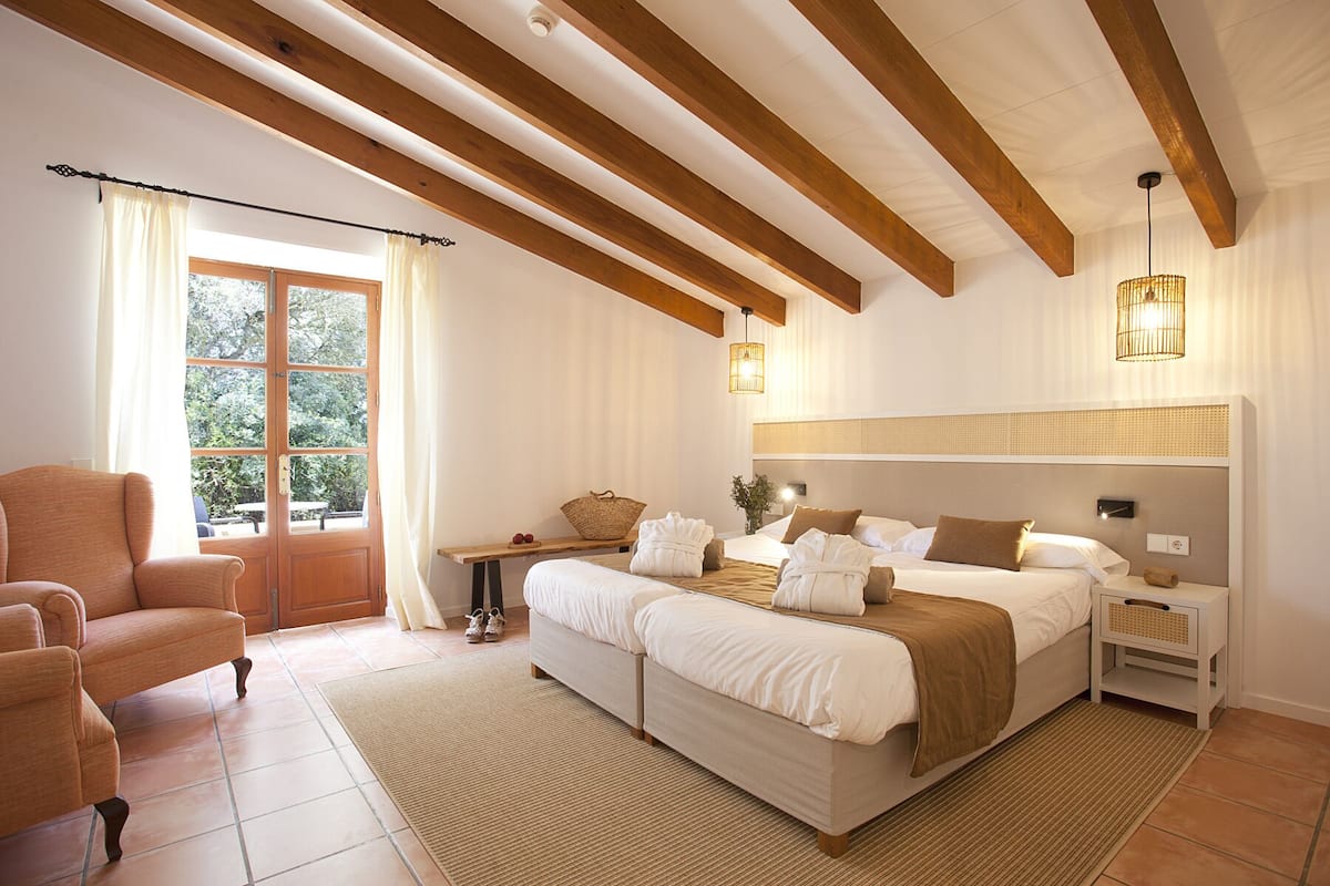 A bedroom with a large bed, a nightstand, a bench with towels, and a window with curtains.
