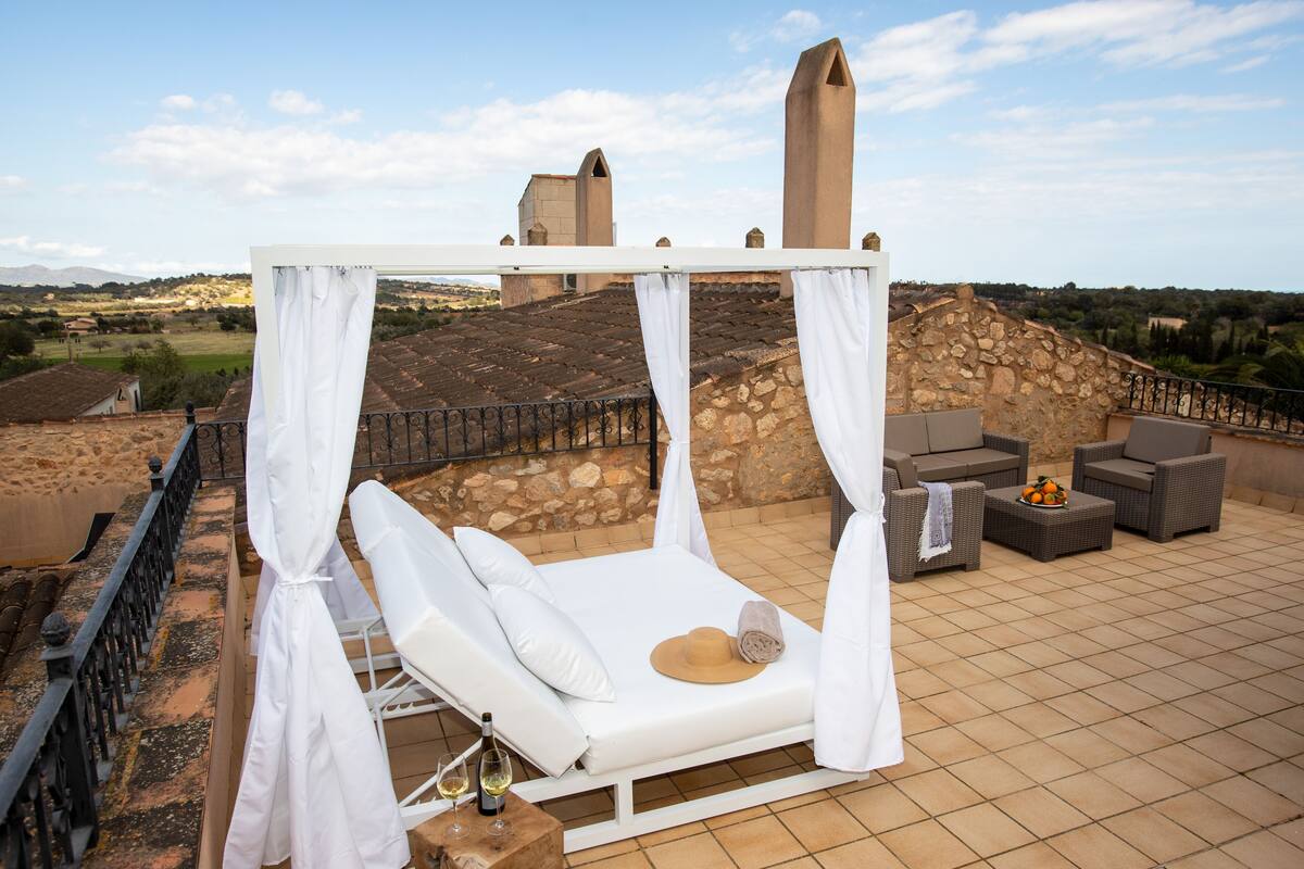 A rooftop terrace with a white canopy bed, outdoor furniture, and a view of the countryside.