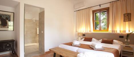 Habitación de hotel con dos camas, un banco, ducha y ventana con cortinas.