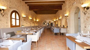 Ein Restaurant mit Steinwänden, Holzbalken und mehreren Tischen mit Stühlen.