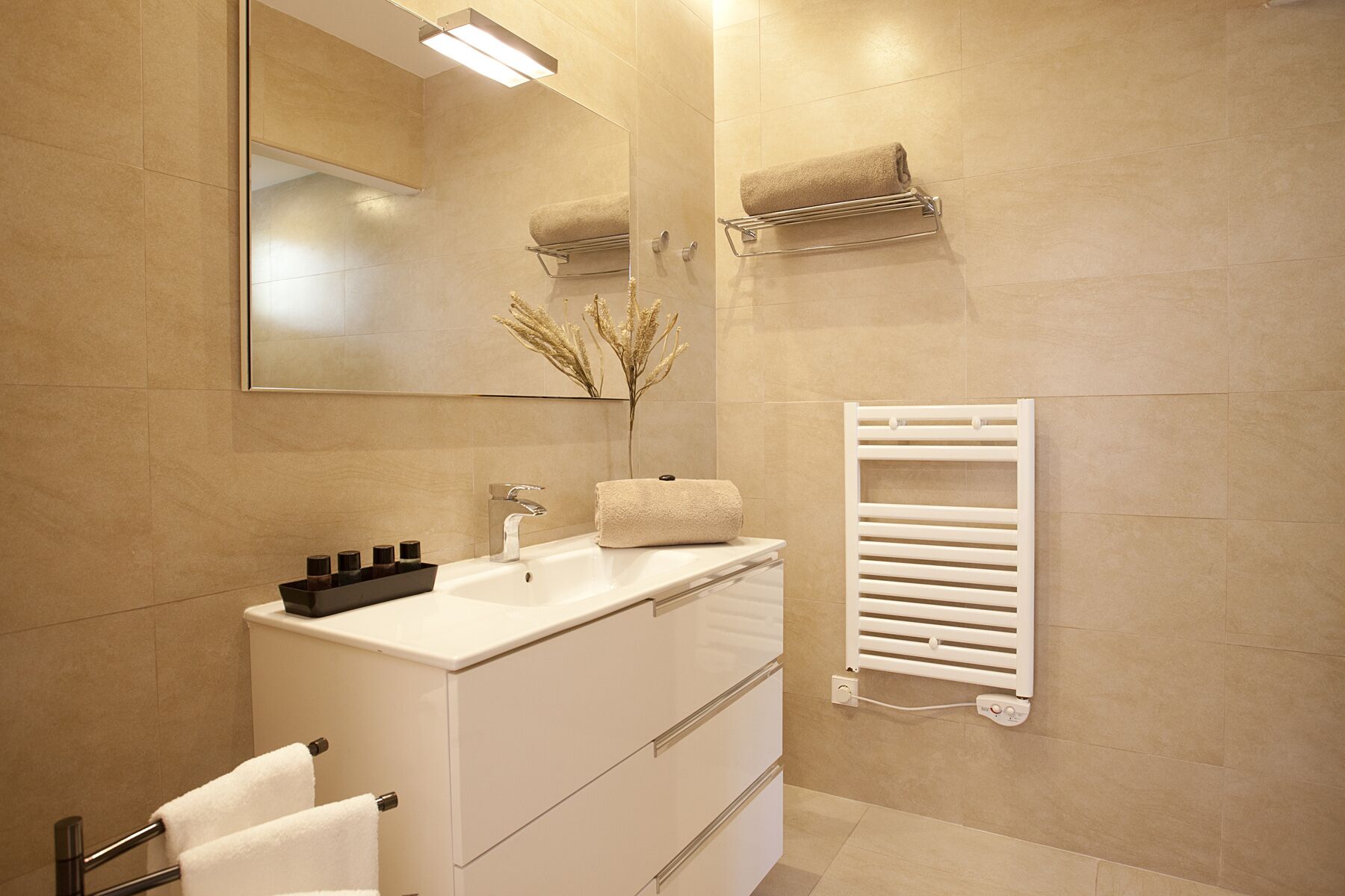 A modern bathroom with a white vanity, a large mirror, a towel rack, and a built-in towel warmer.