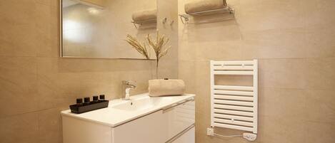 A modern bathroom with a white vanity, a large mirror, a towel rack, and a built-in towel warmer.