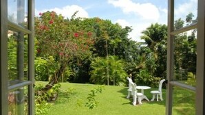 A view through a glass door of a lush garden with a white outdoor seating area. - The Bungalow at Pantiya Estate (Matugama)